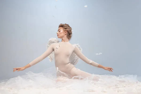 Piękna młoda dziewczyna, pełna wdzięku balerina w obrazie anioła ze skrzydłami siedzącymi na chmurze odizolowanej na białym szarym tle studia. Sztuka, show, balet, piękno, koncepcja inspiracji. — Zdjęcie stockowe
