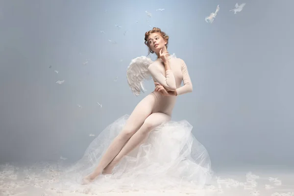 Belle jeune fille, gracieuse ballerine à l'image d'ange avec des ailes assises sur un nuage isolé sur fond de studio gris blanc. Art, spectacle, ballet, beauté, concept d'inspiration. — Photo
