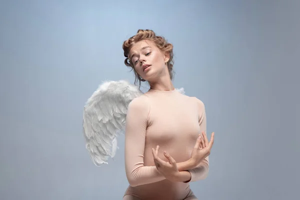 Portret pięknej, szczupłej młodej dziewczyny, pełna wdzięku balerina w obrazie anioła ze skrzydłami siedzącymi na chmurze odizolowanej na białym szarym tle pracowni. — Zdjęcie stockowe