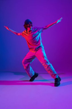 Neon ışıklarıyla dans salonunda renkli arka planda hip-hop dansı yapan sportif genç adam. Gençlik kültürü, hareket, tarz ve moda, aksiyon.