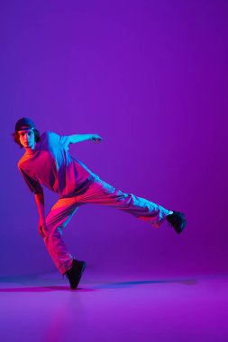 Renkli arka planda dans pistinde neon ışıklarıyla hip-hop dansı yapan şık sporcu çocuk. Gençlik kültürü, hareket, tarz ve moda, aksiyon.