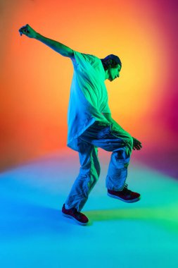 Genç adamın yakın plan portresi, şık kıyafetler giymiş hip-hop dansçısı renkli arka planda, neon ışıklı dans salonunda izole edilmiş..