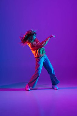 Renkli arka planda dans pistinde neon ışıklarıyla hip-hop dansı yapan şık bir kız. Gençlik kültürü, hareket, tarz ve moda, aksiyon.