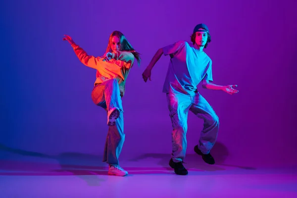 二人のダンサー,若い男と女性ダンスヒップホップでカジュアルスポーツ若い服でグラデーション紫ピンクの背景にダンスホールでネオン光. — ストック写真