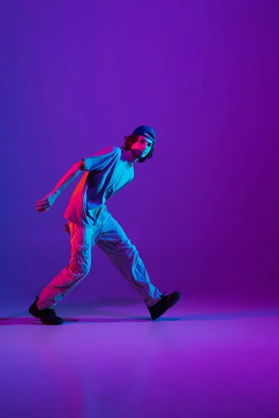 Stijlvolle sportieve jongen dansend hip-hop in stijlvolle kleding op kleurrijke achtergrond in de danszaal in neon licht. Jeugdcultuur, beweging, stijl en mode, actie. — Stockfoto