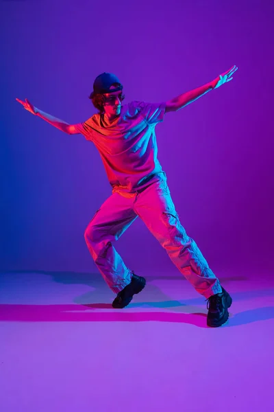 Joven deportivo bailando hip-hop con ropa elegante sobre fondo colorido en el salón de baile con luz de neón. Cultura juvenil, movimiento, estilo y moda, acción. — Foto de Stock