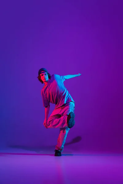 Elegante chico deportivo bailando hip-hop con ropa elegante sobre fondo colorido en el salón de baile en luz de neón. Cultura juvenil, movimiento, estilo y moda, acción. — Foto de Stock