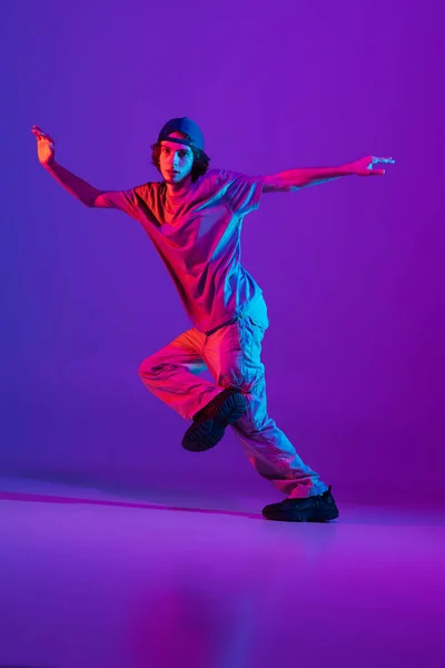 Stylischer sportlicher Junge tanzt Hip-Hop in stylischer Kleidung vor buntem Hintergrund im Tanzsaal in Neonlicht. Jugendkultur, Bewegung, Stil und Mode, Action. — Stockfoto