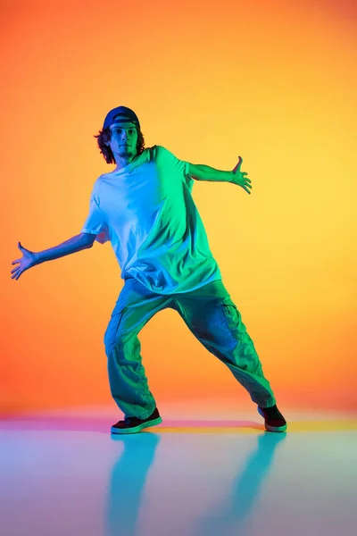 Close-up portret van jonge man, hip-hop danser in stijlvolle kleding in actie geïsoleerd op kleurrijke achtergrond in de danszaal in neon licht. — Stockfoto