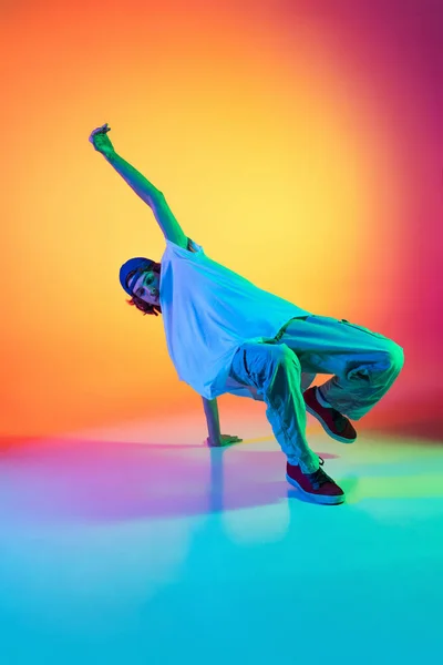 Εννοιολογικό πορτραίτο του νεαρού άνδρα, hip-hop χορευτή με κομψά ρούχα σε δράση απομονωμένο σε πολύχρωμο φόντο στην αίθουσα χορού στο νέον φως. — Φωτογραφία Αρχείου