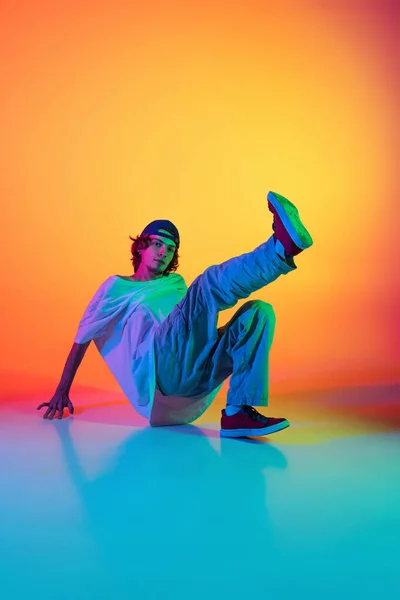 Close-up portret van jonge man, hip-hop danser in stijlvolle kleding in actie geïsoleerd op kleurrijke achtergrond in de danszaal in neon licht. — Stockfoto