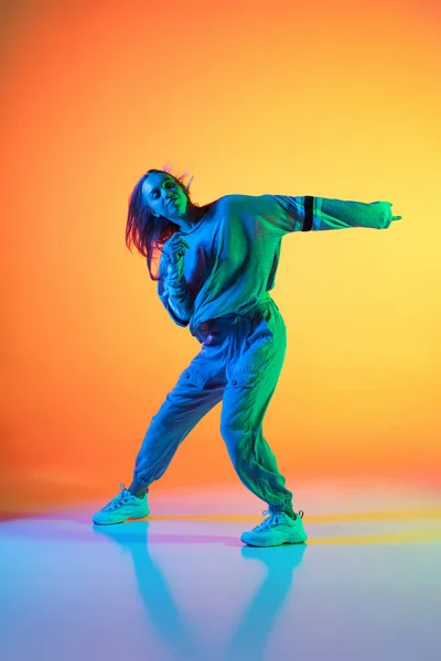 Een Kaukasisch sportief meisje dansend hip-hop in stijlvolle kleding op kleurrijke achtergrond in de danszaal in neon licht. Jeugdcultuur, beweging, stijl en mode, actie. — Stockfoto