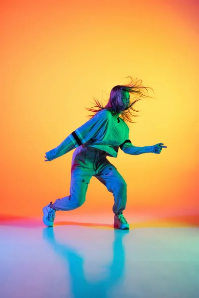 Jong sportief meisje dansend hip-hop in stijlvolle kleding op kleurrijke achtergrond in de danszaal in neon licht. Jeugdcultuur, beweging, stijl en mode, actie. — Stockfoto