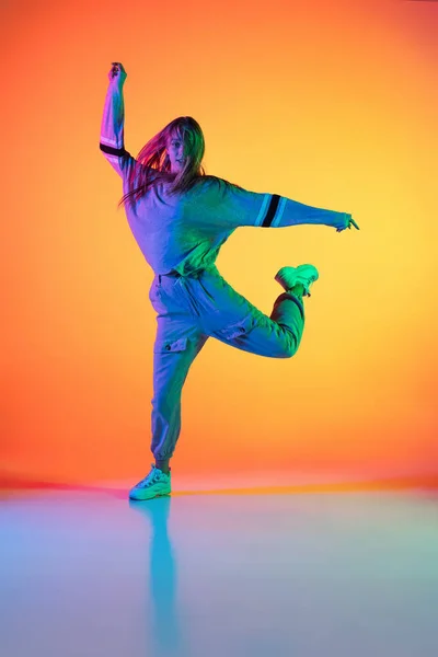 Retrato de jovem menina esportiva dançando hip-hop em roupas elegantes em fundo colorido no salão de dança em luz de néon. Cultura da juventude, movimento, estilo e moda, ação. — Fotografia de Stock