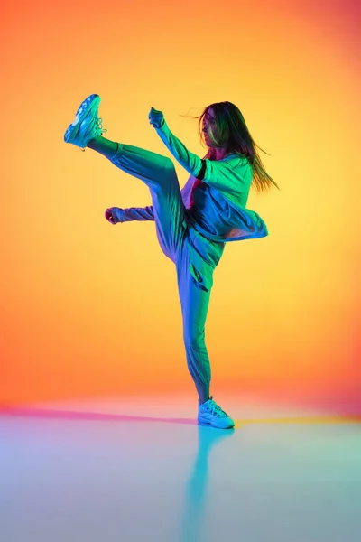 Portret van jong sportief meisje dansend hip-hop in stijlvolle kleding op kleurrijke achtergrond in danszaal in neon licht. Jeugdcultuur, beweging, stijl en mode, actie. — Stockfoto