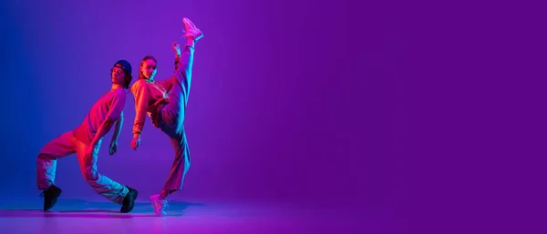 Een flyer. Twee dansers, jonge man en vrouw dansen hip-hop in casual sport jeugd kleding op gradiënt paars roze achtergrond in danszaal in neon licht. — Stockfoto