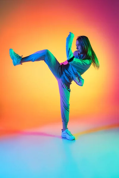 Deportiva chica flexible bailando hip-hop en ropa elegante sobre fondo colorido en el salón de baile en luz de neón. Cultura juvenil, movimiento, estilo y moda, acción. — Foto de Stock