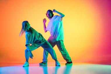 Genç dansçılar, şık duygusal kız ve oğlan, neon ışıklarıyla dans salonundaki çok renkli arka planda günlük spor gençlik kıyafetleriyle hip-hop dansı yapıyorlar..