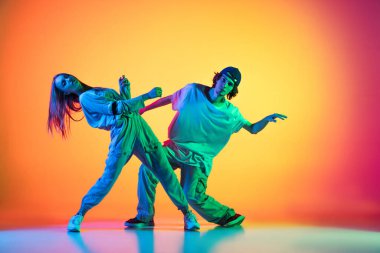 İki dansçı, genç bir kız ve erkek, neon ışıklarıyla dans salonundaki çok renkli arka planda günlük spor gençlik kıyafetleriyle hip-hop dansı yapıyorlar..