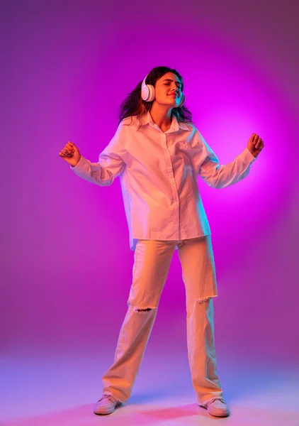 Portret Latynoski pięknej dziewczyny słuchającej muzyki odizolowanej na fioletowym, liliowym tle studia w neonowym świetle. Pojęcie ludzkich emocji, wyraz twarzy — Zdjęcie stockowe