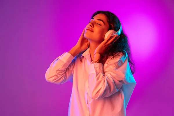 Portrét krásné Latino dívka poslech hudby izolované na fialové, šeříkové barvy studio pozadí v neonovém světle. Pojem lidské emoce, výraz obličeje — Stock fotografie