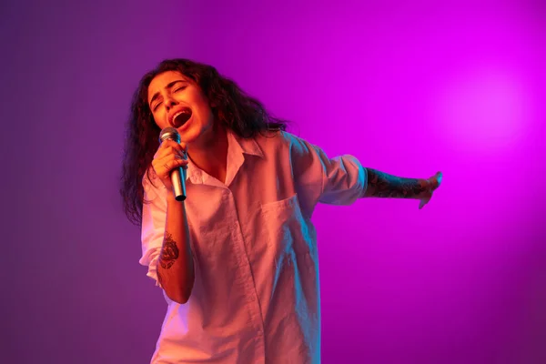 Bright fashionable portrait of beautiful happy girl signing isolated on purple, lilac color studio background in neon light. Concept of human emotions, facial expression — Stock Photo, Image