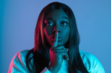 Neon ışıklarıyla mavi stüdyo arka planında izole edilmiş uzun düz saçlı Afrikalı çekici bir kadının yakın plan portresi. İnsan duyguları kavramı