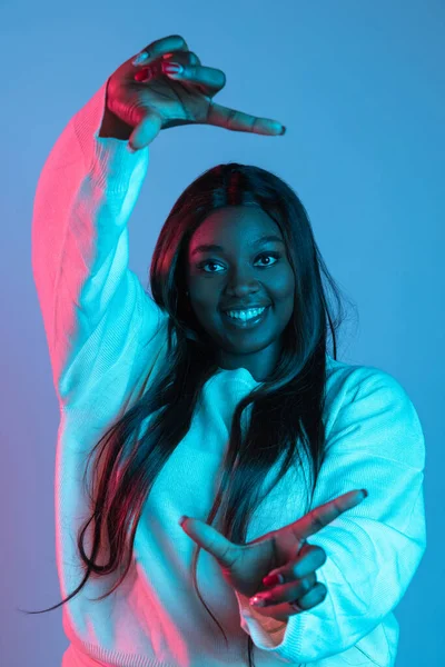Eine schöne afrikanische Frau mit langen glatten Haaren gestikuliert isoliert auf blauem Studiohintergrund in Neonlicht. Konzept menschlicher Emotionen — Stockfoto
