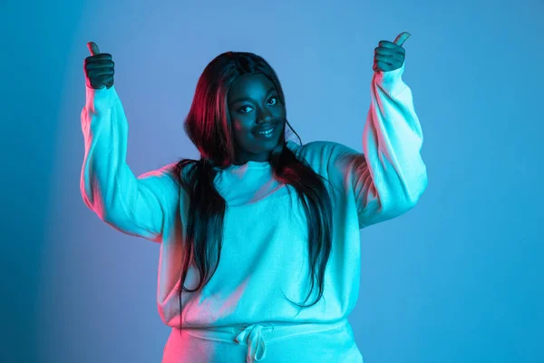 Uzun düz saçlı güzel bir Afrikalı kadın mavi stüdyo arka planında neon ışıkta izole edilmiş. İnsan duyguları kavramı — Stok fotoğraf