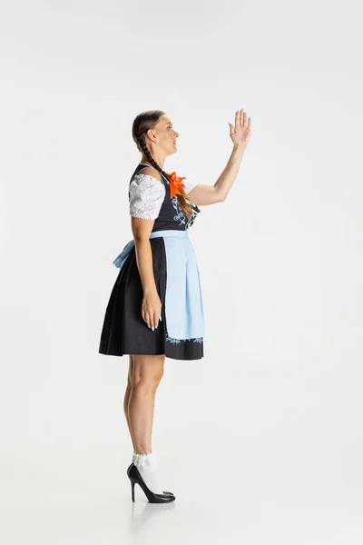 Full-length portrait of beautiful woman, waitress in traditional Austrian or Bavarian costume standing alone isolated over white background. Side view — Stock Photo, Image