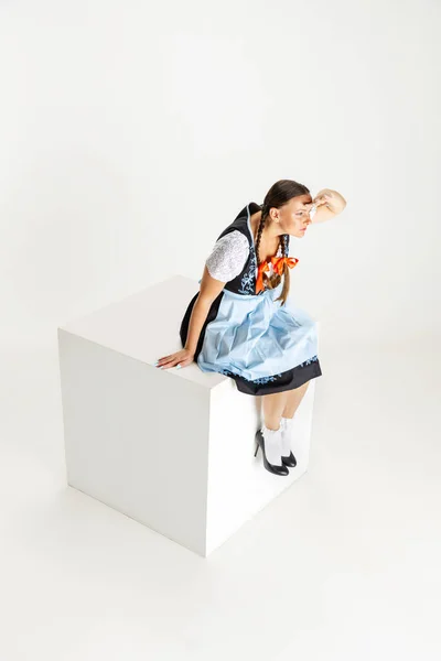 Attraktiv vit kvinna, servitris i traditionell österrikisk eller bayersk kostym sitter på stor låda isolerad över vit bakgrund. Begreppet Oktoberfest — Stockfoto