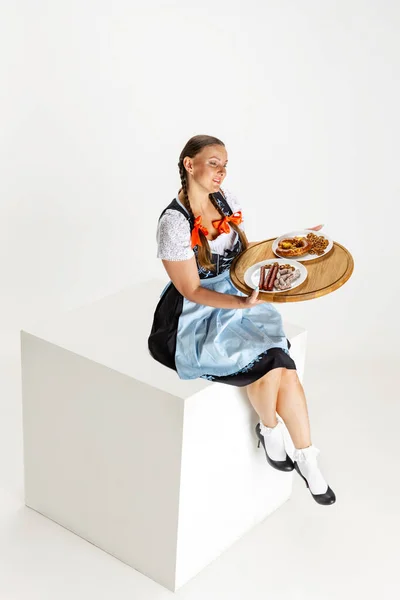 Stúdió lövés vonzó nő, pincérnő hagyományos osztrák vagy bajor jelmez ül tálca hatalmas doboz elszigetelt fehér háttér. Oktoberfest koncepció — Stock Fotó