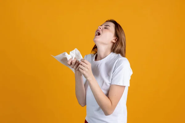 Ein junges Mädchen niest und hat einen Schnupfen isoliert auf gelbem Studiohintergrund. Konzept menschlicher Emotionen, Mimik, Gesundheit und Medizin — Stockfoto