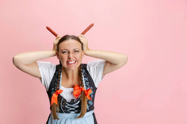 Nette hübsche Wiesn-Frau, Kellnerin in traditionellem bayerischem oder deutschem Dirndl mit Spaß auf rosa Studiohintergrund. — Stockfoto