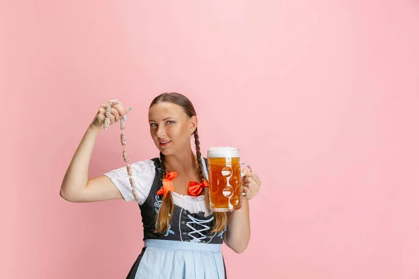 Adorable mujer Oktoberfest, camarera con un dirndl tradicional bávaro o alemán sosteniendo un vaso de cerveza de un litro aislado sobre fondo rosa estudio. — Foto de Stock
