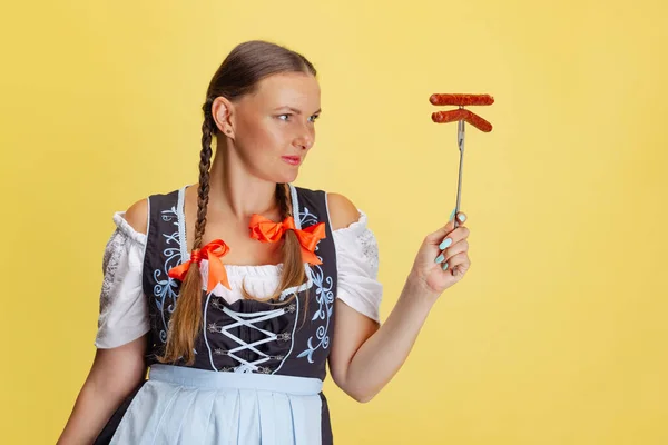 Komiczny portret pięknej kobiety Oktoberfest, kelnerki ubranej w tradycyjny bawarski lub niemiecki dirndl izolowane na żółtym tle studio. — Zdjęcie stockowe