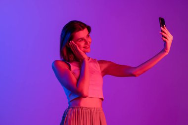 Mor, eflatun renkli stüdyo arka planında telefon kullanan beyaz bir kız. İnsan duyguları kavramı, yüz ifadesi, kozmetik, gençlik