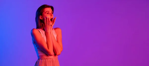 Estúdio tiro de menina caucasiana jovem isolado no fundo do estúdio roxo em luz de néon. Conceito de emoções humanas, expressão facial, cosméticos, juventude — Fotografia de Stock