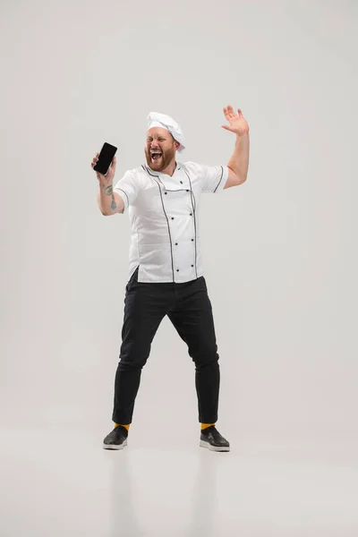 Happy chef-kok, kok in uniform met behulp van telefoon geïsoleerd op witte achtergrond. Concept van baan, beroep, humor, gezichtsuitdrukkingen — Stockfoto