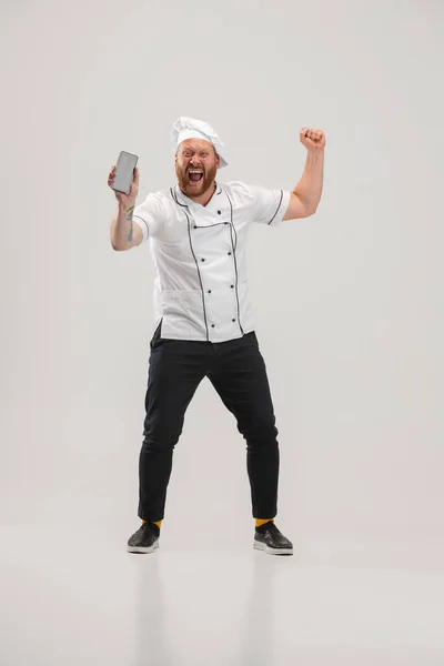 Happy chef-kok, kok in uniform met behulp van telefoon geïsoleerd op witte achtergrond. Concept van baan, beroep, humor, gezichtsuitdrukkingen — Stockfoto