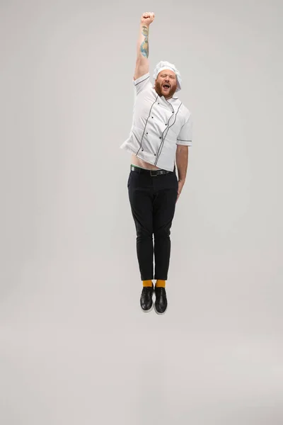 One Caucasian bearded man, chef in uniform jumping high isolated on white background. Concept of job, occupation, humor. — Stock Photo, Image