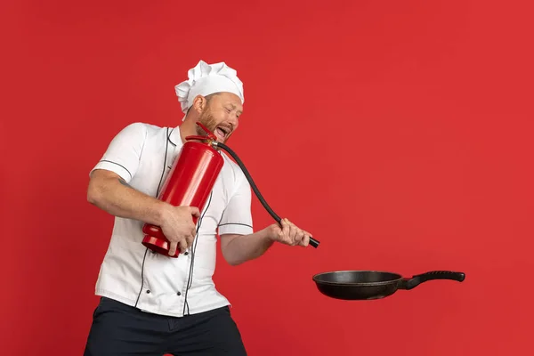 Comic portret van hadsome baardman, kok, mannelijke chef-kok in wit uniform plezier geïsoleerd op rode studio achtergrond. Begrip werk, beroep, humor. — Stockfoto