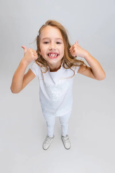 Високий кут зору красивої маленької дівчинки з довгим волоссям в сучасному стильному вбранні позує ізольовано на білому фоні студії. Концепція щасливого дитинства . — стокове фото