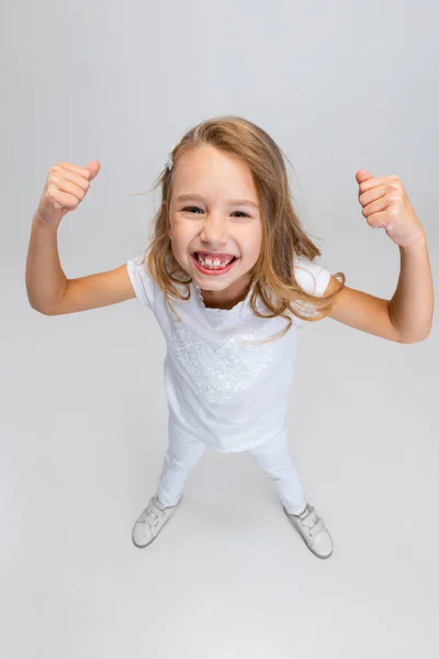 Vue grand angle de belle petite fille aux cheveux longs dans une tenue moderne et élégante posant isolée sur fond de studio blanc. Concept d'enfance heureuse. — Photo