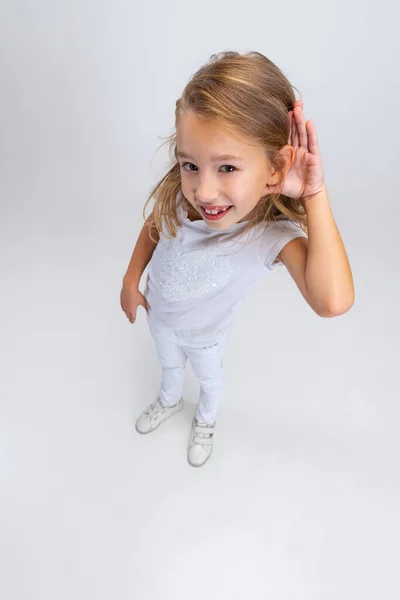 Jedna krásná holčička s dlouhými vlasy v moderním stylovém oblečení pózuje izolované na bílém pozadí studia. Šťastné dětství koncept. — Stock fotografie