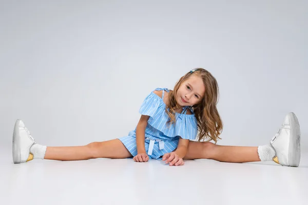 Beautiful little girl in blue holiday outfit sitting on floor isolated on white studio background. Happy childhood concept. Sunny child. — Stock Photo, Image