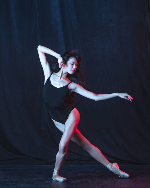 Young and graceful female ballet dancer in motion isolated on dark background in neon light. Art, motion, action, flexibility, inspiration concept.