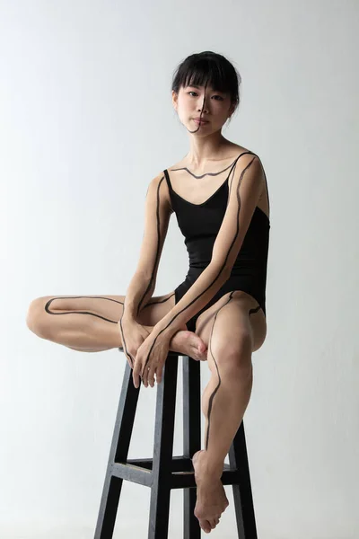 Ritratto di giovane adorabile ballerina giapponese seduta sul seggiolone e pensante isolata su sfondo grigio chiaro da studio. Bellezza, line art, concetto di mondo interiore. — Foto Stock