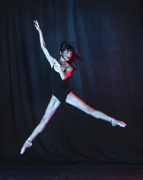 Joven y elegante bailarina de ballet en movimiento aislada sobre fondo oscuro en luz de neón. Arte, movimiento, acción, flexibilidad, concepto de inspiración. — Foto de Stock