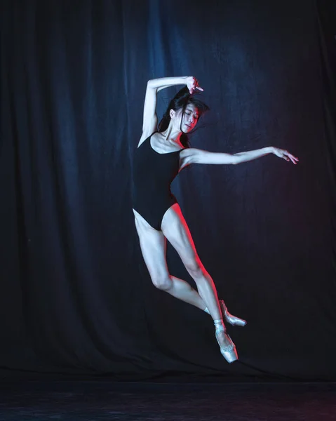 ネオンの光の中で暗い背景に隔離された動きの若い優雅な女性バレエダンサー。芸術、運動、行動、柔軟性、インスピレーションの概念. — ストック写真